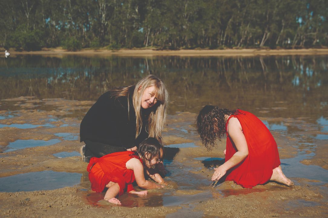 An adult female playing with two female children in the mud at the beach